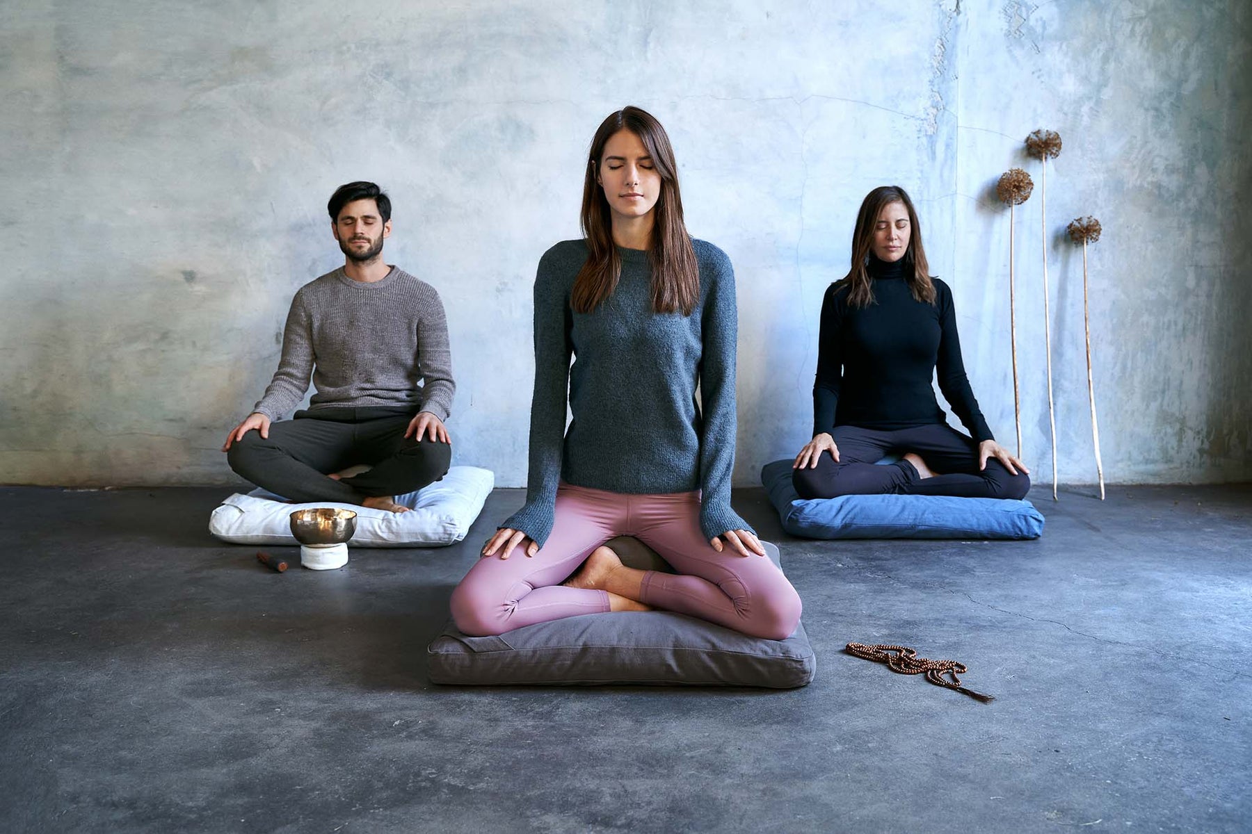 renoo meditation cushions | three meditation pillow sets on floor with practitioners. renoo zafu and zabuton cushions shown in colors vanilla (off-white), slate (dark gray) and teal (Indian teal/blue).